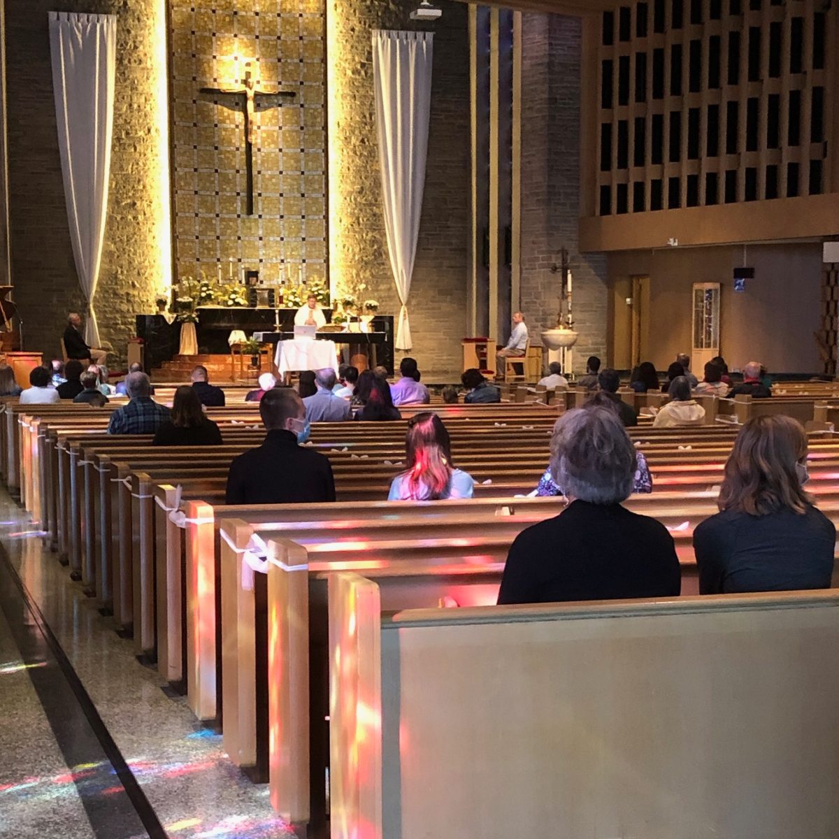 Parishioners gathered for Mass, viewed from behind, with the altar and crucifix ahead.